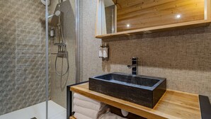 Une salle de bain moderne avec une douche en verre, un meuble-lavabo en bois avec un évier noir et des serviettes soigneusement pliées.