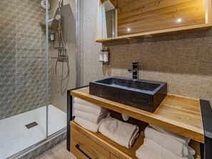 Ein modernes Badezimmer mit Glasdusche, einem Holzlager für Waschbecken mit schwarzem Becken und ordentlich gefalteten Handtüchern.
