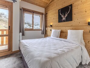 Ein Zimmer mit Holzwänden, einem Bett, einem Fenster mit Vorhängen, einer Wandlampe und einem Bild einer Hirschschädel.