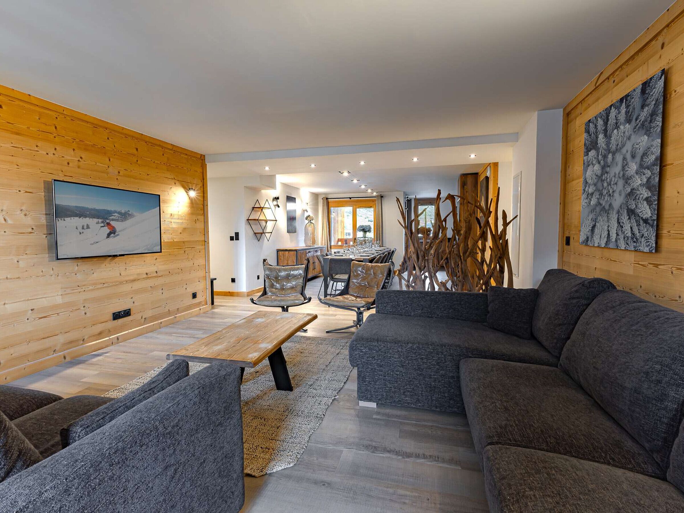 A modern living room with a wooden wall, a TV, a sofa, and a dining area.