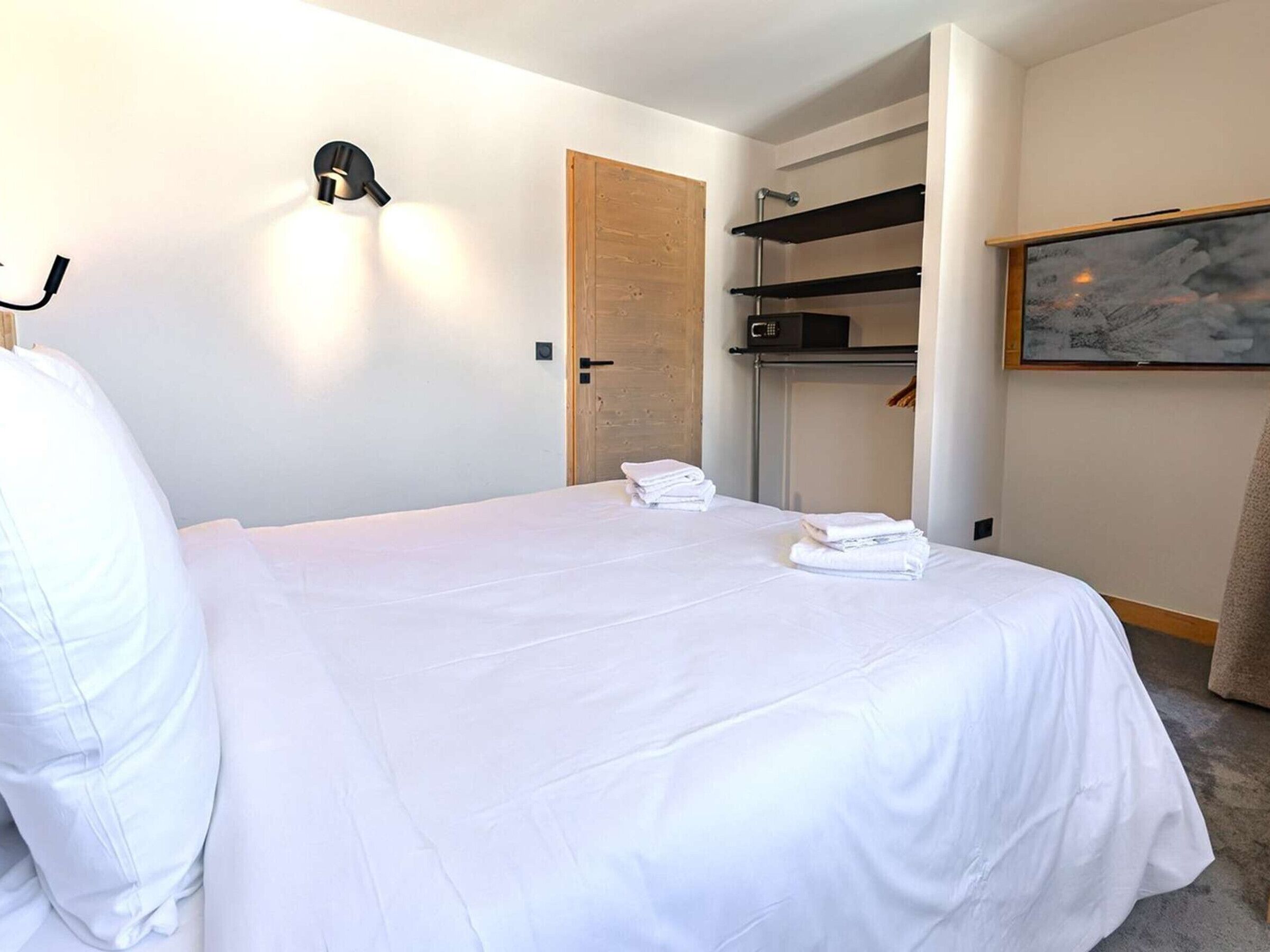 Een hotelkamer met een bed, een deur, een magnetron, een plank en een schilderij aan de muur.