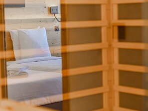 Ein Bett mit weißer Bettwäsche und Kissen, ein hölzerner Kopfteil und eine Steckdose an der Wand.
