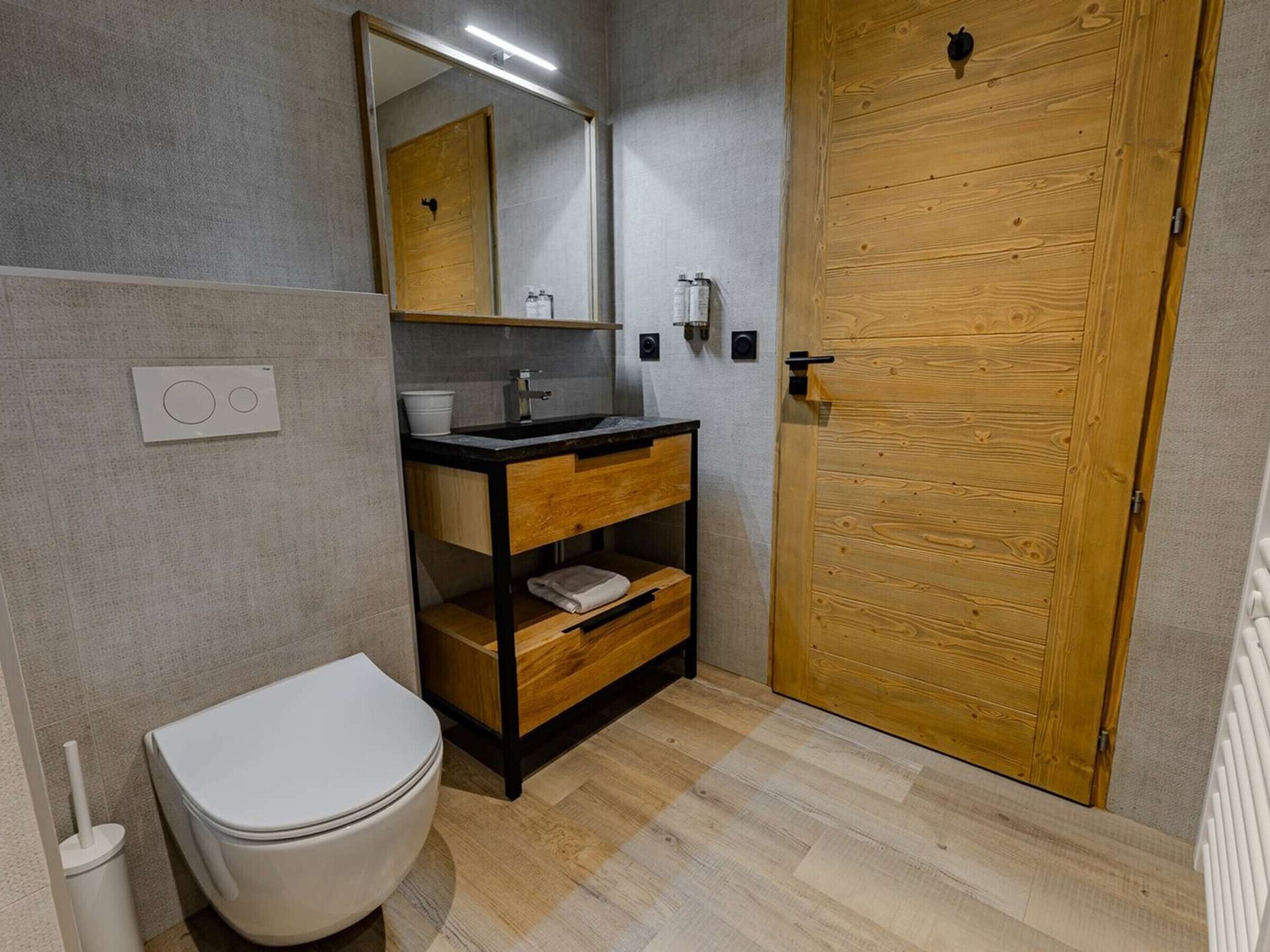 Ein Badezimmer mit Toilette, Waschbecken, Spiegel, Holztür und Handtuchablage.