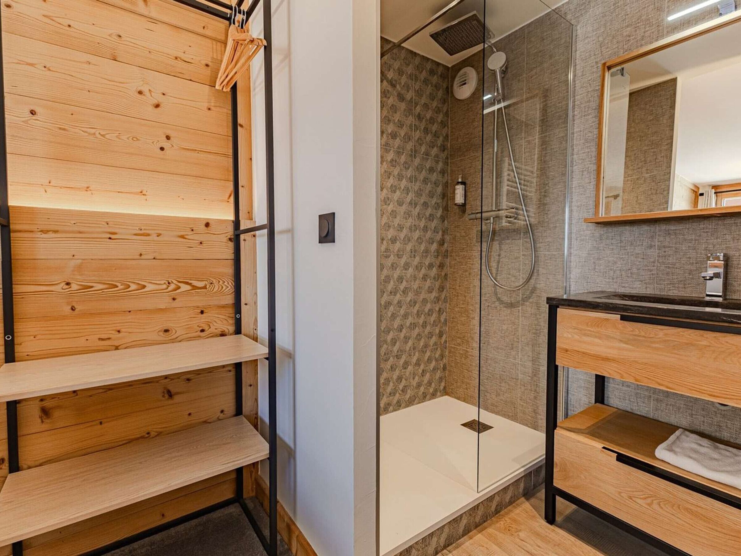 Une salle de bain moderne avec des étagères en bois, une cabine de douche en verre et un miroir au-dessus du lavabo.