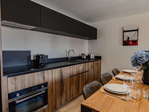 A modern kitchen with dark cabinetry, a wooden island, and a dining area with a table set for four. - Spacious apartment, 8-10 guests, in Belle Plagne (Belle Plagne)