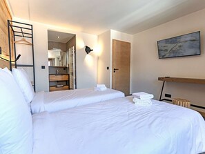 Ett hotellrum med två sängar, en garderob i trä, en spegel, en handduksställning och en tavla på väggen.