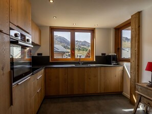 A kitchen with wooden cabinets, a double sink, and a window with a mountain view. - Modern mountain chalet - 9 guests (Plagne Soleil)