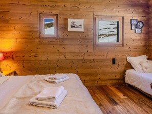 Ein Zimmer in einer Holzhütte mit einem Bett, zwei Fenstern und gerahmten Bildern an der Wand.