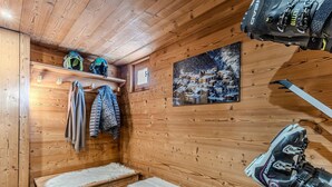 Una baita di legno con panche, un supporto per sci e un quadro raffigurante un villaggio innevato.