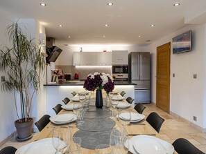 Un espace repas moderne avec un îlot central, une cuisine en arrière-plan et une plante en pot sur la gauche.
