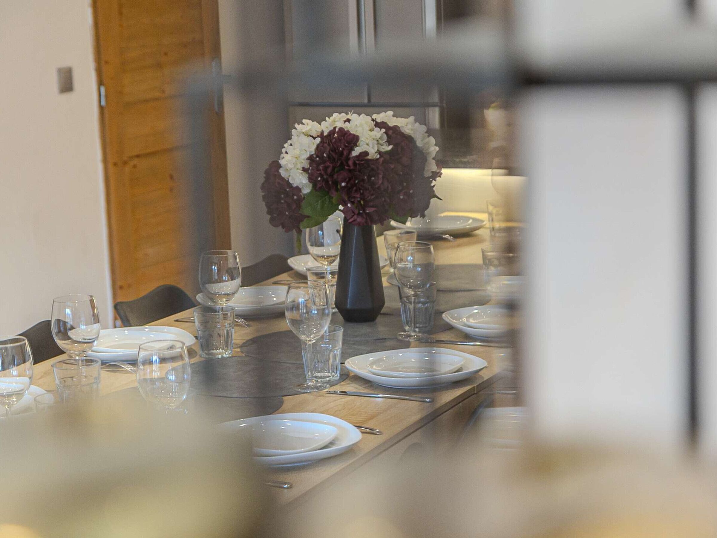 Une table à manger dressée avec des assiettes, des verres et un vase rempli de fleurs.