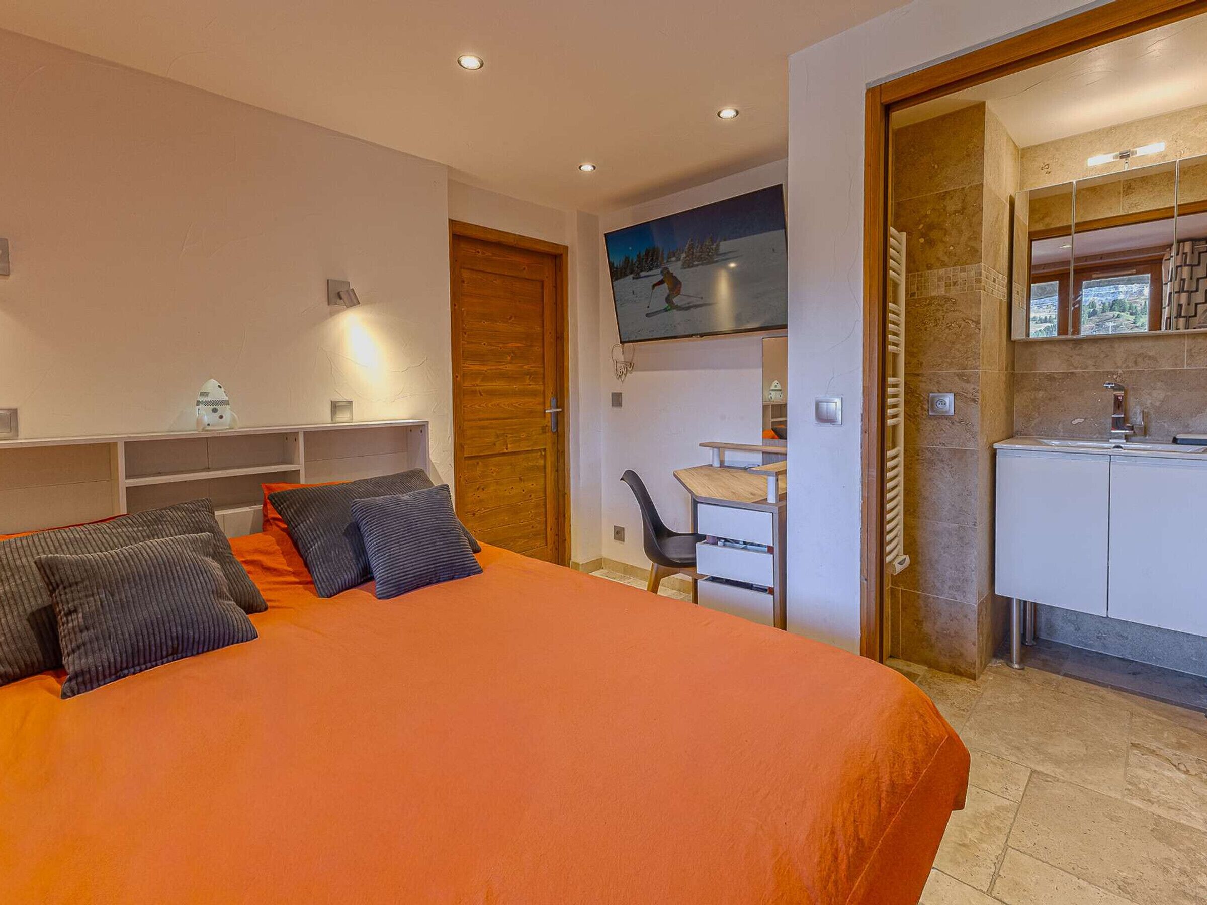 A modern bedroom with a bed, a desk, and a bathroom.