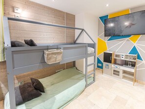 Cama litera con bolsa de almacenamiento, televisión y kitchenette en una habitación con paneles de madera.