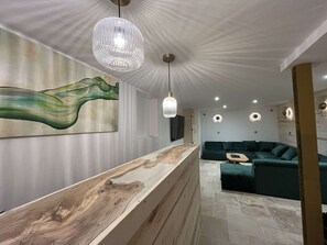 A modern interior with a wooden reception desk, a green sofa, pendant lights, and a wall-mounted artwork. - Luxurious slopeside apartment - 15 guests (Belle Plagne)