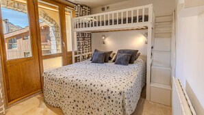 Een slaapkamer met een stapelbed, een groot raam en uitzicht op een stenen gebouw.