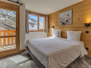 Un dormitorio con cabecera de madera, cama con ropa de cama blanca, ventana con vistas a montañas nevadas y un cuadro de un oso polar en la pared.