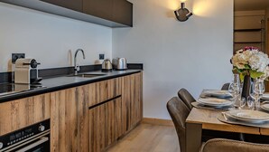 A modern kitchen with wooden cabinets, a built-in oven, a sink, and a dining area with a table set for two. - Cozy apartment - 6 guests, near slopes (Belle Plagne)