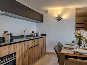 A modern kitchen with wooden cabinets, a built-in oven, a sink, and a dining area with a table set for two. - Cozy apartment - 6 guests, near slopes (Belle Plagne)