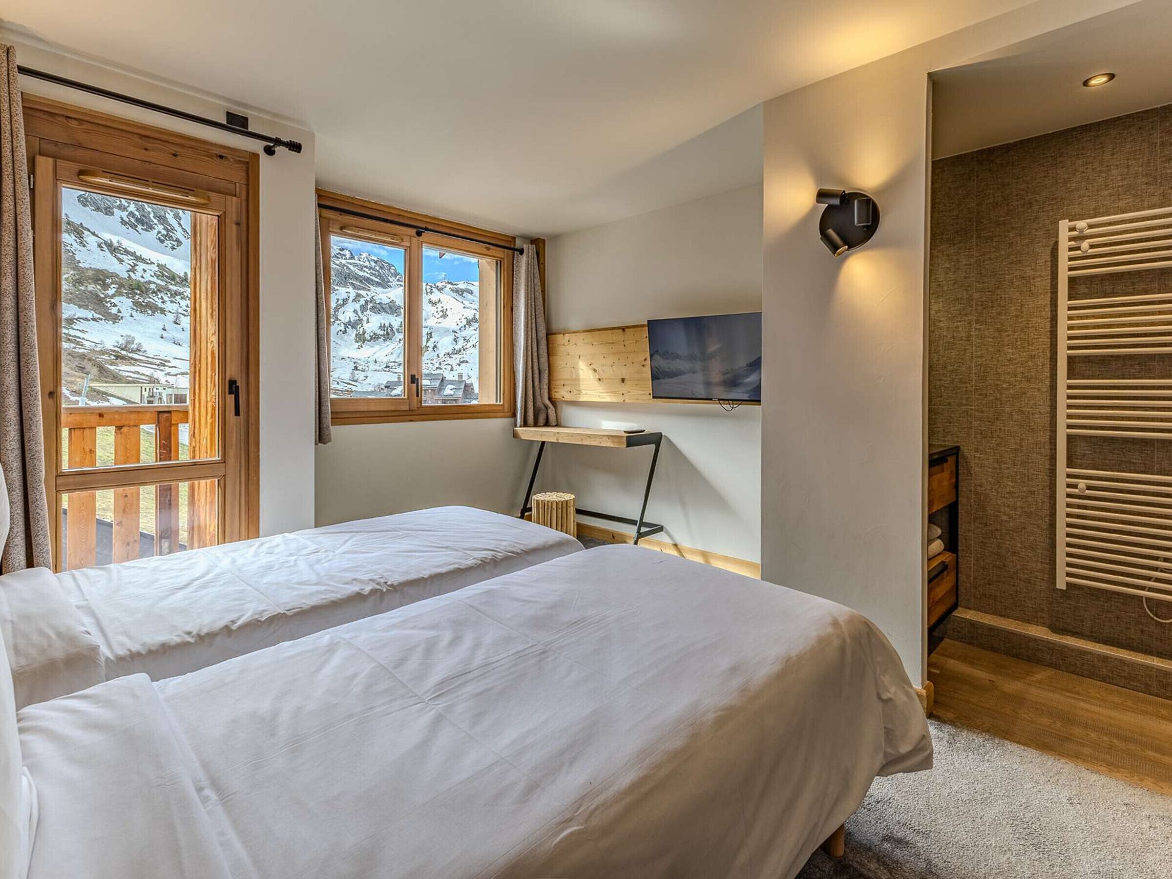 Un dormitori amb dos llits, televisió, escriptori i vista a muntanyes nevades.