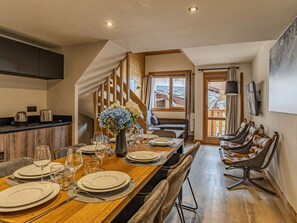 A dining area with a wooden table set for a meal, a sofa, and a chair with a unique design. - Spacious apartment, mountain view - 8 guests (Belle Plagne)