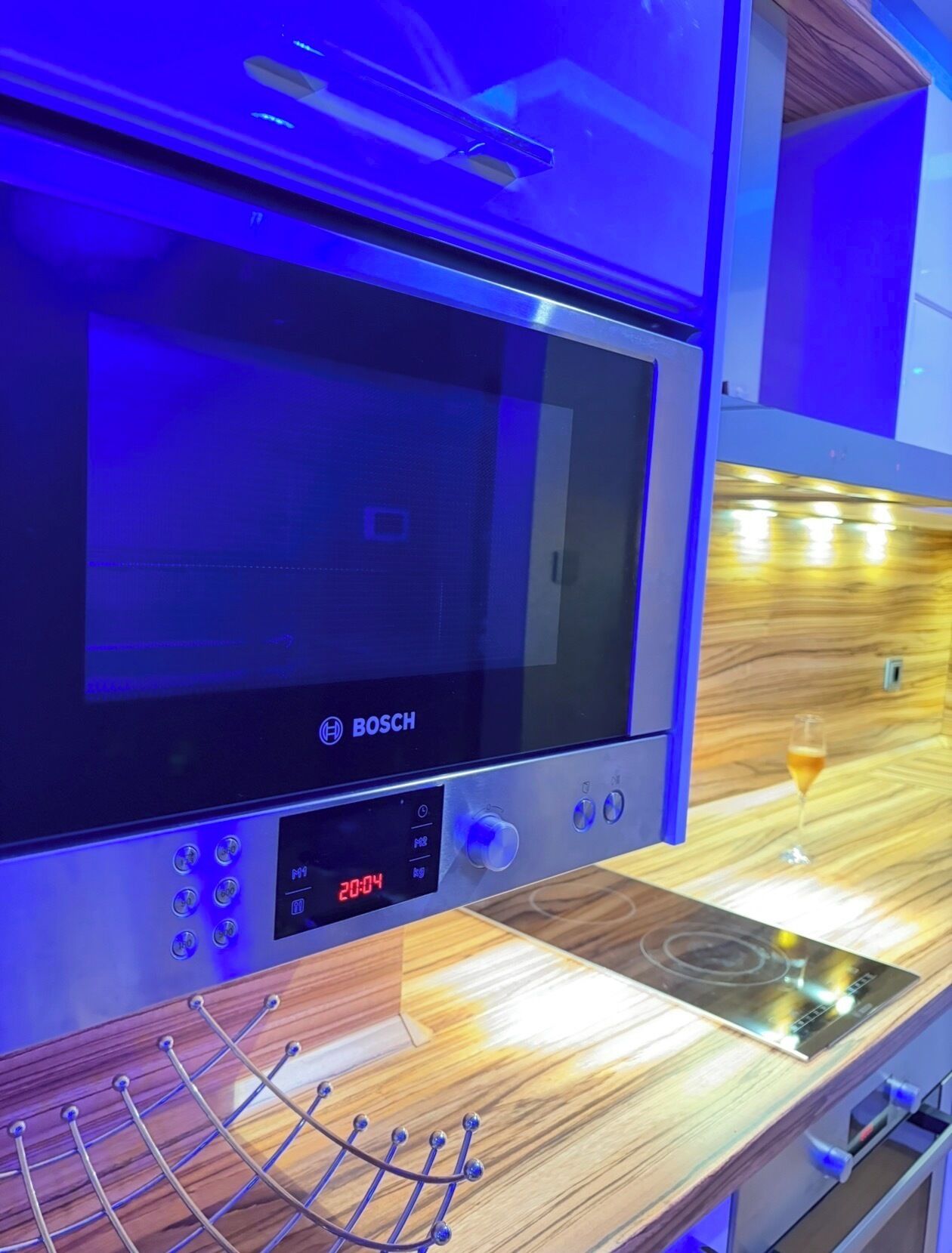 A kitchen with a Bosch microwave, a digital clock, and a wine glass on the counter.