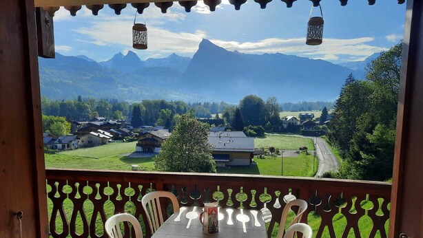 A balcony with a table and chairs, overlooking a mountainous landscape with houses and greenery. - Apartment with mountain view, pets welcome - 4 guests (Morillon Village)