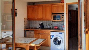 A compact kitchen with wooden cabinets, a microwave, a washing machine, and a tiled backsplash. - Apartment with mountain view, pets welcome - 4 guests (Morillon Village)