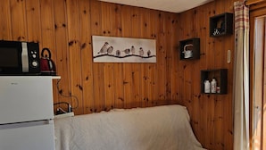 A cozy room with wooden walls, a white sofa, a small refrigerator, and a wall-mounted shelf with decorative items. - Apartment with mountain view, pets welcome - 4 guests (Morillon Village)