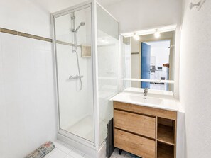 Ein modernes Badezimmer mit einer Glaskabine zur Dusche, einem weißen Waschbecken und einem Spiegel darüber.