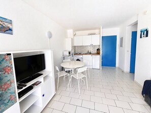 Ein kleiner Wohnbereich mit Fernseher, Essplatz, Küche und einer blauen Tür.