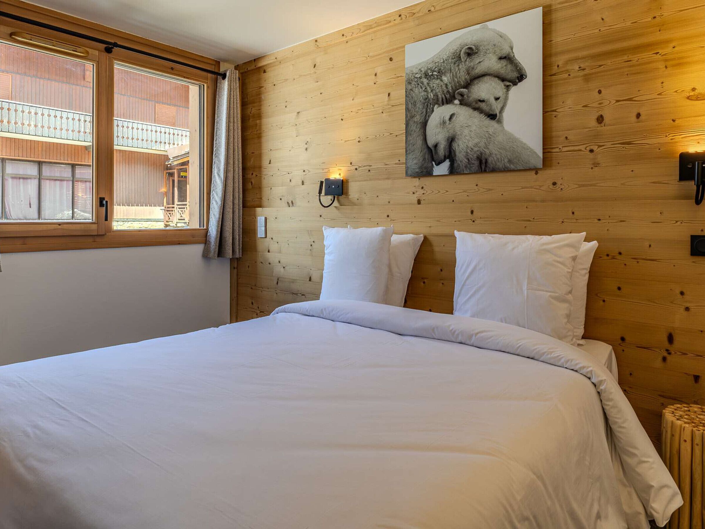 Ein Schlafzimmer mit einem Holz-Kopfteil, einem Bett mit weißer Bettwäsche, einem Fenster mit Vorhängen und einer Wandleuchte.