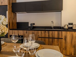 Eine moderne Küche mit Holzschränken, einer schwarzen Arbeitsplatte, einer Edelstahlspüle und einer Kaffeemaschine.
