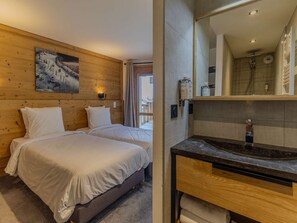 Hotellihuone, jossa on kaksi sänkyä, puinen pääty, taulu, kylpyhuone, jossa on pesuallas ja peili, sekä suihku.