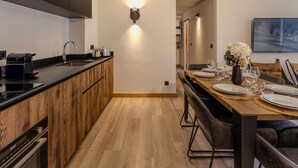 A modern kitchen with a wooden island, a dining area with a wooden table and chairs, and a wall-mounted light fixture. - Cozy apartment in Belle Plagne - 6 guests (Belle Plagne)