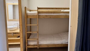 En køjeseng med en trætrap, en hvid vask og et spejl i et lille rum.