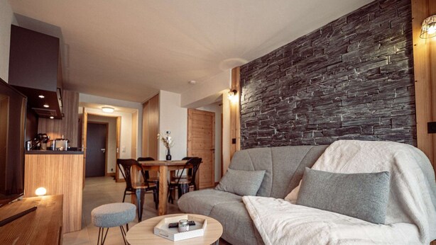 En moderne stue med en stenvæg, en sofa, et sofabord og et spiseområde med stole.