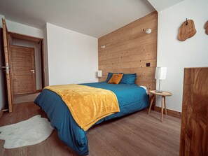 A bedroom with a wooden headboard, a bed with blue bedding, a small bedside table with a lamp, and a white rug. - Modern apartment in the heart of the resort - 6 guests (La Plagne)