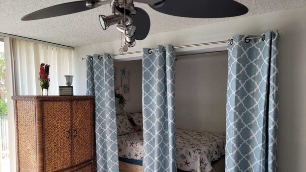 Een slaapkamer met een plafondventilator, een bed met bloemenbeddels en een garderobe.