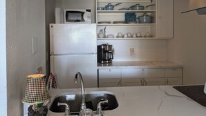 Een kleine keuken met een koelkast, magnetron, koffiezetapparaat en een spoelbak met kraan.