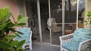 Een overdekt terras met twee rieten stoelen, een ventilator en uitzicht door een glazen deur.