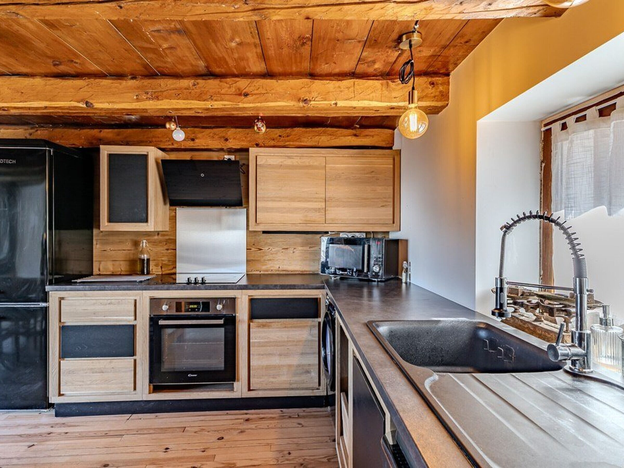 Una cocina moderna con armarios de madera, horno empotrado, microondas y pileta de acero inoxidable.