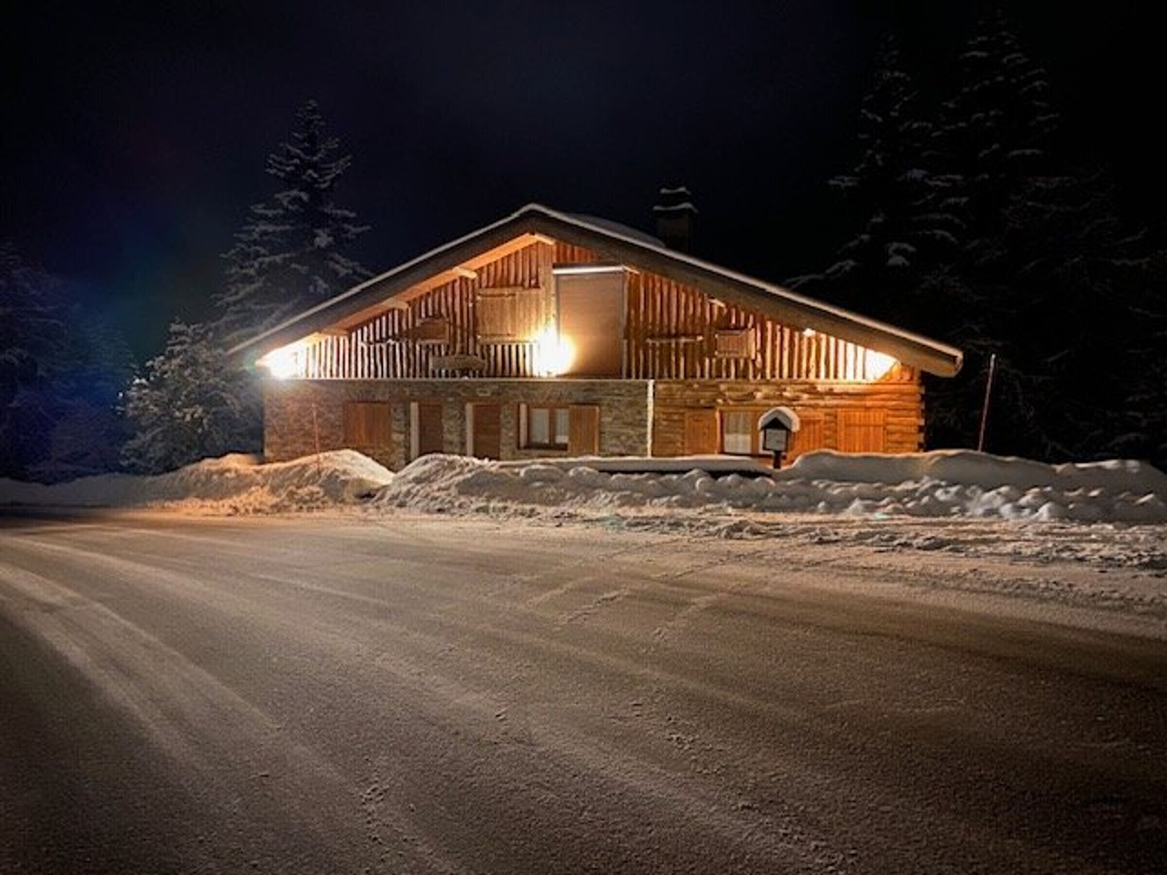 A log cabin with a wooden exterior, a stone foundation, and a snow-covered driveway.