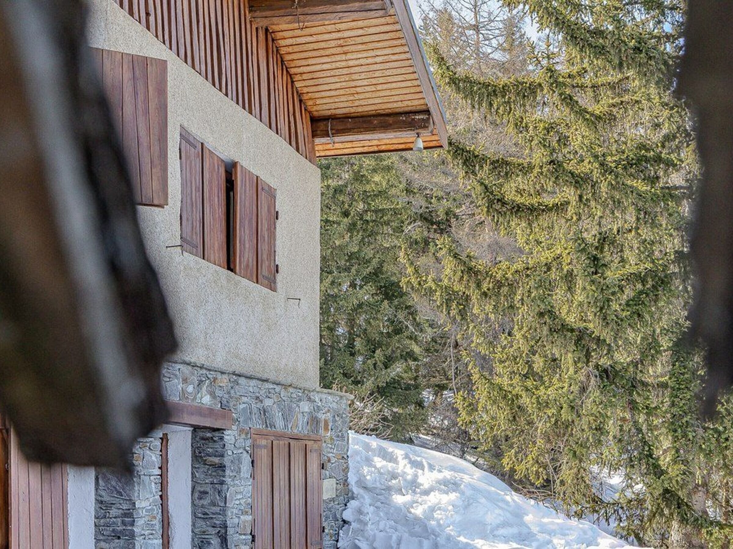 A modern two-story building with wooden shutters, stone walls, and a view of a snowy landscape with trees.