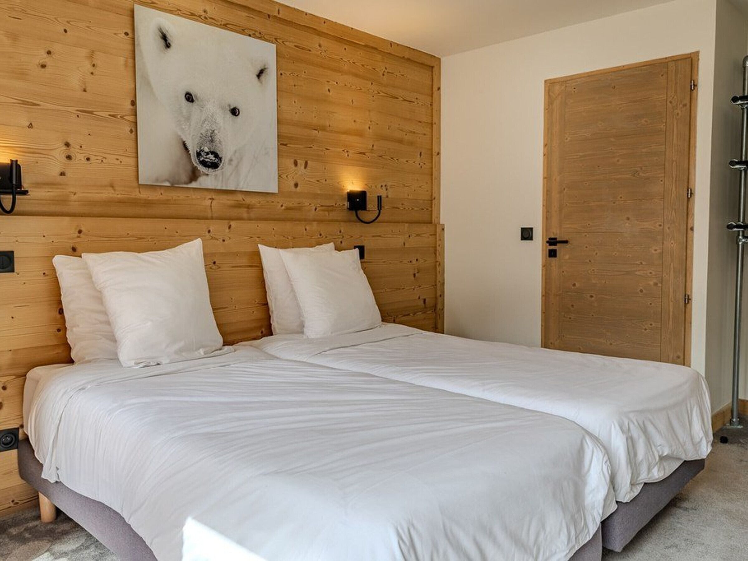 Een slaapkamer met een houten hoofdbord, een groot wit sprei en een vastgeplakt beeld van een ijsbeer.