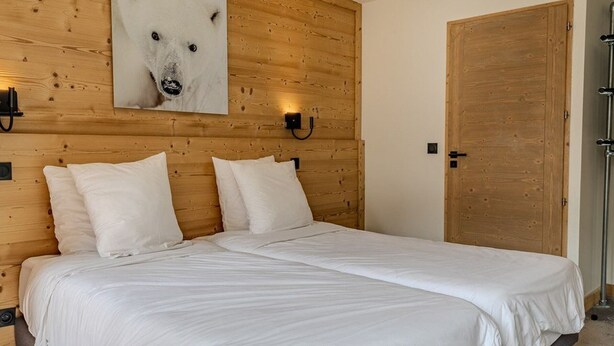 Een slaapkamer met een houten hoofdbord, een groot wit sprei en een vastgeplakt beeld van een ijsbeer.
