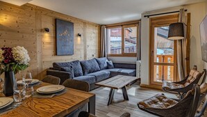 Een knus woongedeelte met een houten wand, een bank, een eettafel gedekt met borden en glazen, en een stoel.