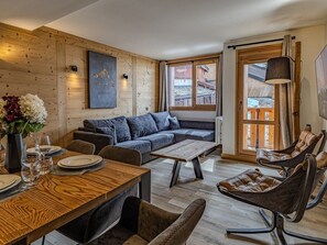 Ein gemütlicher Wohnbereich mit einer Holzwand, einem Sofa, einem Esstisch mit Tellern und Gläsern sowie einem Sessel.