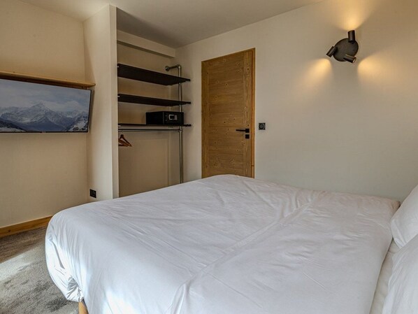 Una camera da letto con un letto, un armadio, una televisione a parete e una porta in legno.