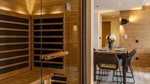 Een modern interieur met een houten sauna, een eethoek met een tafel gedekt voor twee personen, en een houten wand.