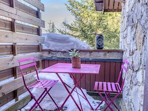 Eine Holzterrasse mit einem rosafarbenen Tisch und Stühlen, einem Blumentopf und einer Steinmauer.